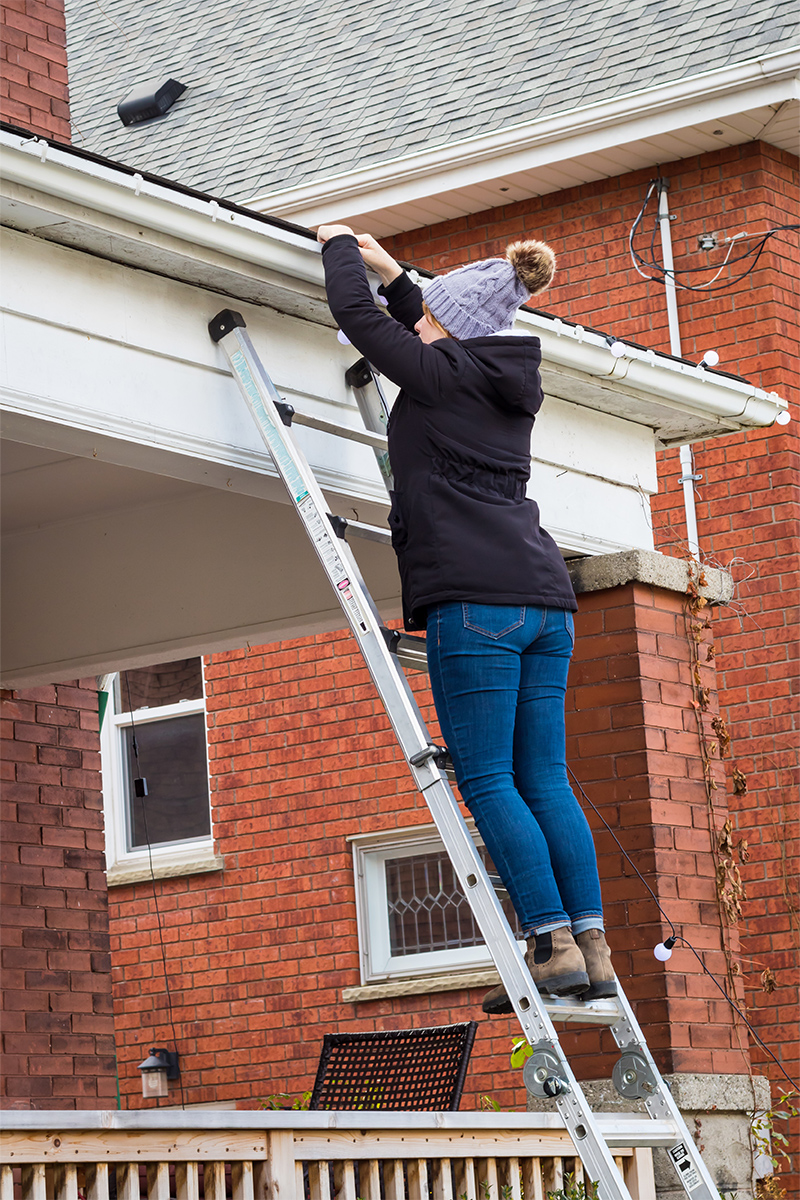 Person hanging up lights while standing on a ladder.