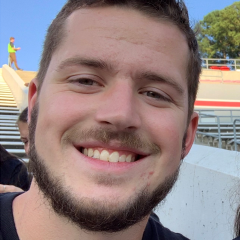 A young man smiles jovially at the camera while at a construction site.