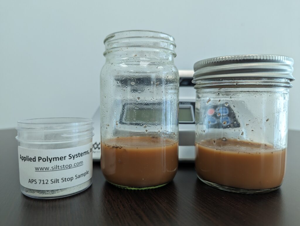 Two glass jars sit beside a chemical flocculant made of polymers. The glass jars are full of brown, sediment-filled water.